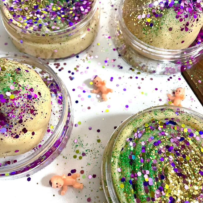 Play dough in a clear container with beautiful green, gold and purple glitter on top with a tiny baby figurine to hide inside